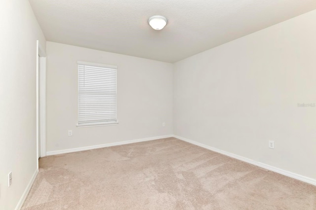 spare room with baseboards, a textured ceiling, and light colored carpet