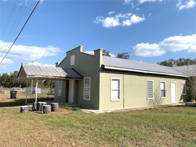 rear view of property featuring a lawn, fence, metal roof, brick siding, and a chimney