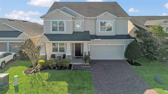 view of front of home featuring a shingled roof, decorative driveway, a front lawn, and stucco siding