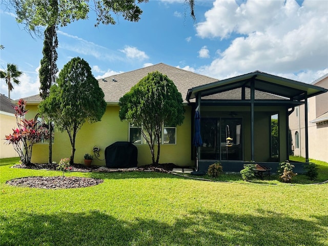 back of property featuring a sunroom, roof with shingles, a lawn, and stucco siding