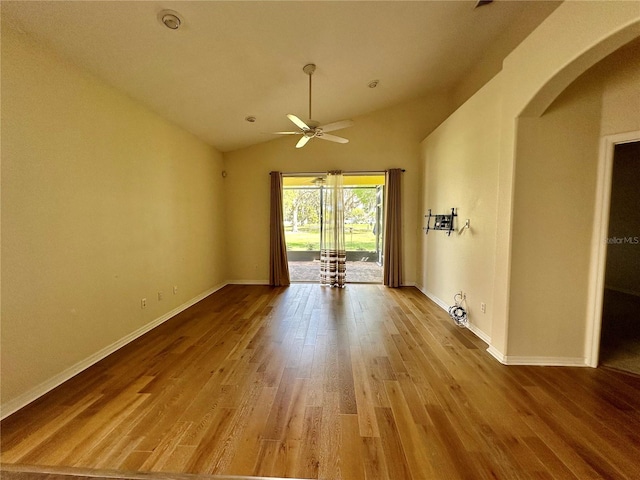 unfurnished room featuring arched walkways, lofted ceiling, wood finished floors, a ceiling fan, and baseboards