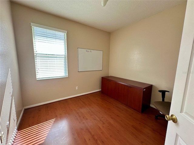 spare room with a textured ceiling, wood finished floors, and baseboards