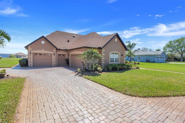 view of front of home with an attached garage, a shingled roof, decorative driveway, stucco siding, and a front yard