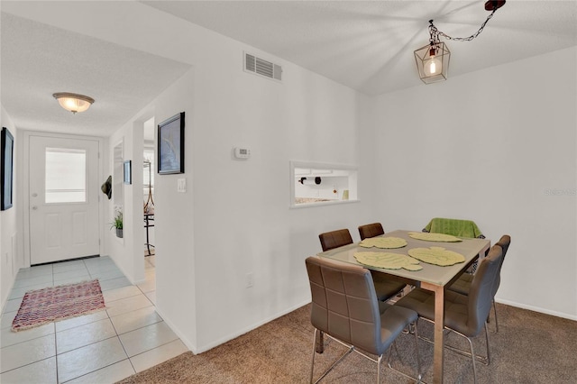 carpeted dining room with baseboards, tile patterned flooring, visible vents, and a textured ceiling