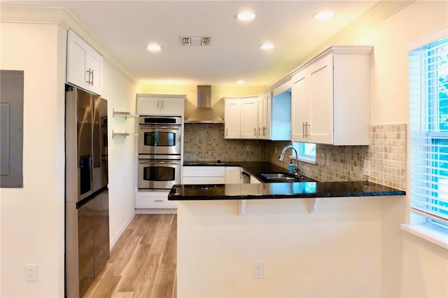 kitchen featuring visible vents, a sink, appliances with stainless steel finishes, a peninsula, and wall chimney range hood