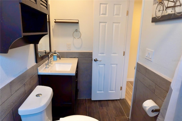 bathroom with wood finish floors, toilet, tile walls, and vanity