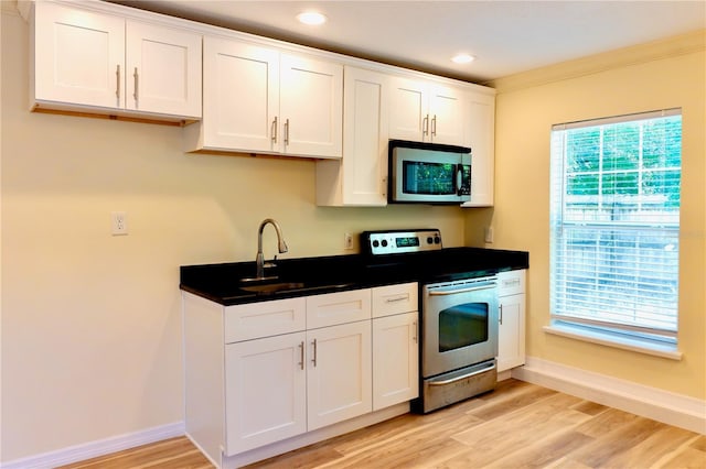 kitchen featuring light wood-style flooring, a sink, appliances with stainless steel finishes, white cabinetry, and dark countertops