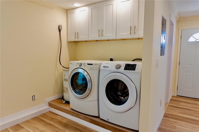 clothes washing area featuring baseboards, washer and clothes dryer, light wood-type flooring, electric panel, and cabinet space