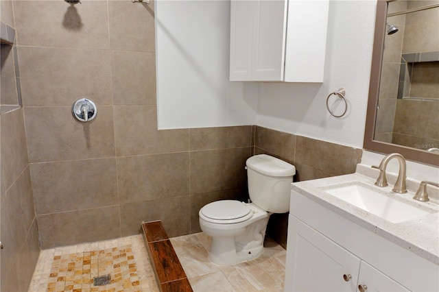 full bath featuring a wainscoted wall, toilet, vanity, tiled shower, and tile walls