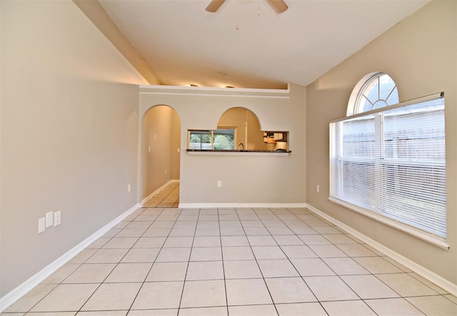 unfurnished room featuring lofted ceiling, arched walkways, light tile patterned flooring, a ceiling fan, and baseboards