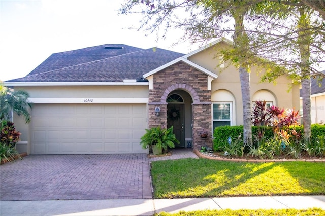 ranch-style home featuring stucco siding, decorative driveway, stone siding, an attached garage, and a shingled roof