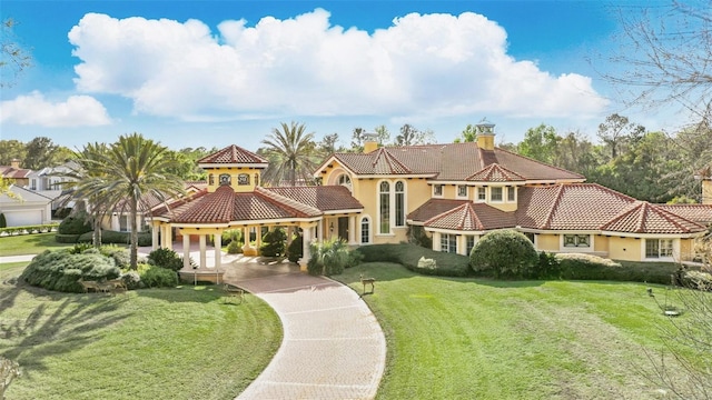 mediterranean / spanish home with a tiled roof, a chimney, a front lawn, and stucco siding