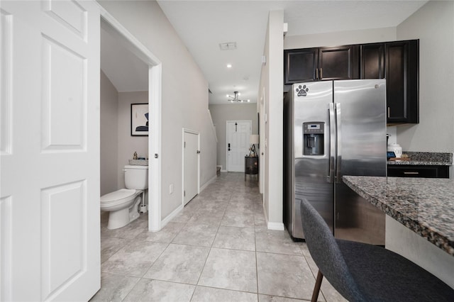 kitchen featuring dark stone counters, light tile patterned flooring, baseboards, and stainless steel fridge with ice dispenser