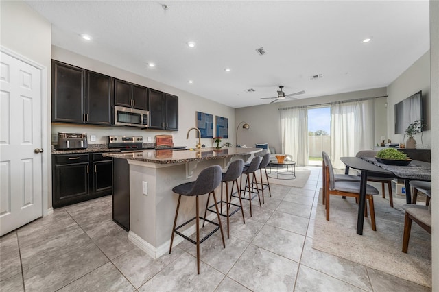 kitchen featuring a kitchen island with sink, visible vents, appliances with stainless steel finishes, dark stone countertops, and a kitchen bar