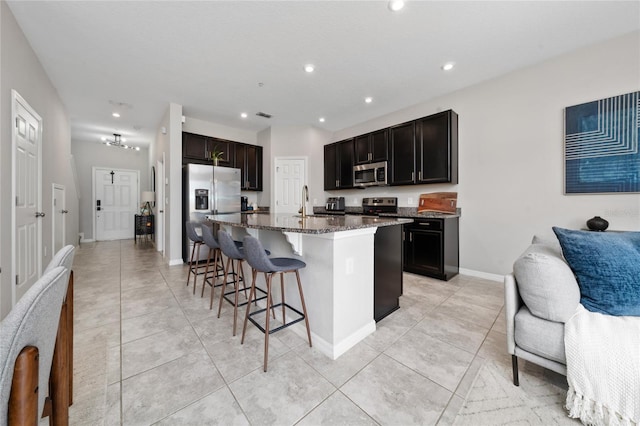 kitchen with a kitchen breakfast bar, open floor plan, appliances with stainless steel finishes, an island with sink, and dark stone countertops