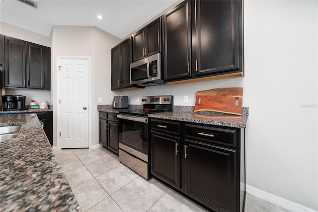 kitchen with baseboards, dark stone counters, appliances with stainless steel finishes, light tile patterned flooring, and recessed lighting