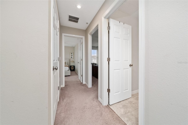 corridor with visible vents, light carpet, and baseboards