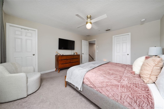 bedroom with a textured ceiling, light carpet, visible vents, a ceiling fan, and baseboards