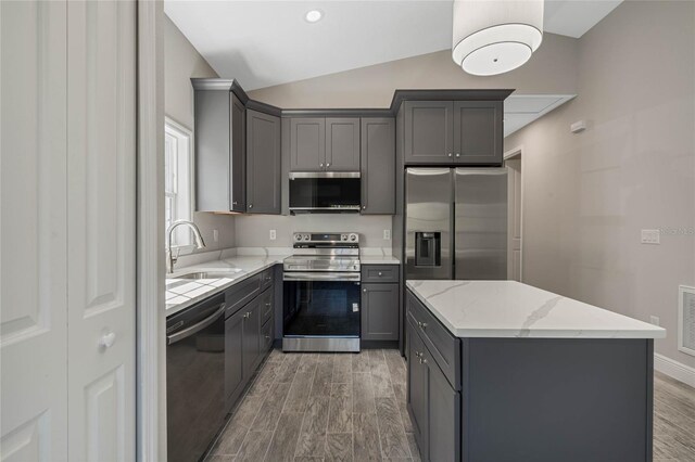 kitchen featuring stainless steel appliances, a sink, vaulted ceiling, light wood-type flooring, and gray cabinets