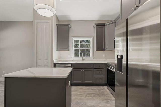 kitchen featuring gray cabinetry, appliances with stainless steel finishes, a center island, wood finish floors, and a sink