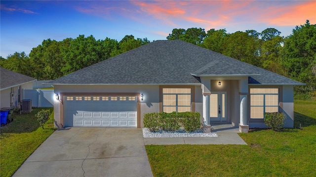 ranch-style home featuring roof with shingles, stucco siding, a yard, a garage, and driveway