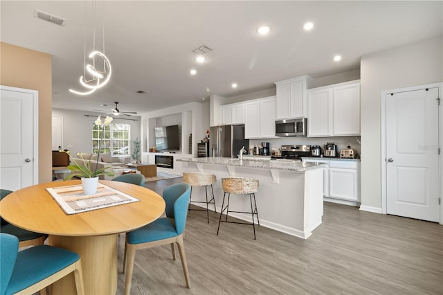 kitchen featuring visible vents, white cabinets, appliances with stainless steel finishes, light wood finished floors, and an island with sink