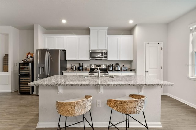 kitchen with beverage cooler, stainless steel appliances, a sink, a kitchen bar, and a center island with sink