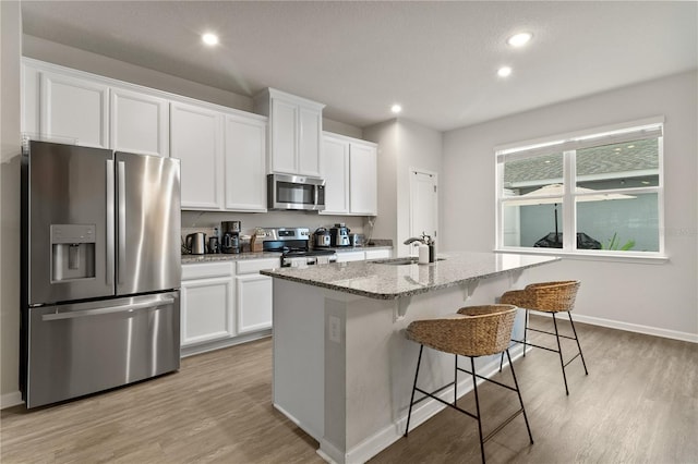 kitchen with stainless steel appliances, white cabinetry, a sink, and a center island with sink