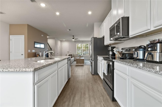 kitchen featuring stainless steel appliances, open floor plan, white cabinets, a kitchen island with sink, and wood finished floors