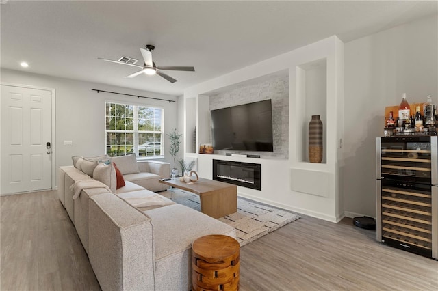 living area featuring ceiling fan, wine cooler, wood finished floors, visible vents, and a glass covered fireplace