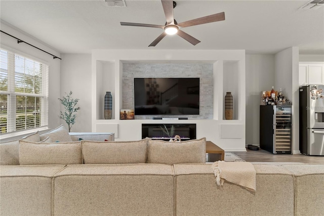 living area featuring wine cooler, a fireplace, wood finished floors, visible vents, and a ceiling fan