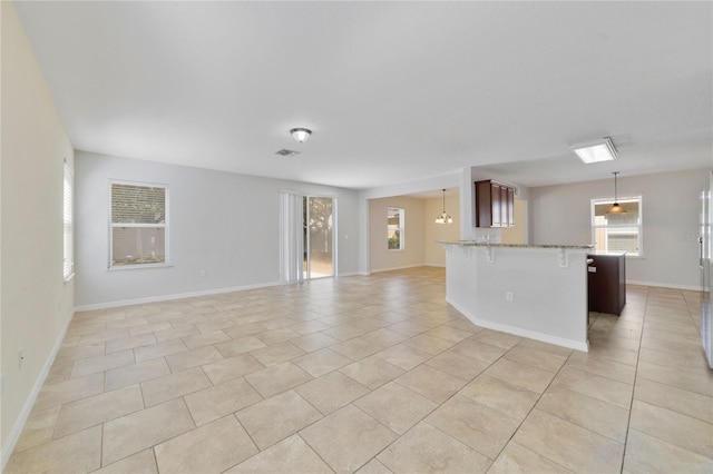 interior space featuring light tile patterned floors, a breakfast bar area, open floor plan, a peninsula, and pendant lighting