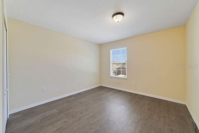 spare room featuring a textured ceiling, dark wood finished floors, and baseboards