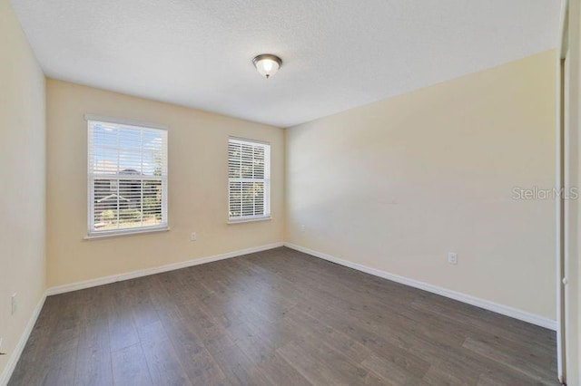 unfurnished room with a textured ceiling, baseboards, and wood finished floors