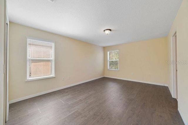 spare room with a textured ceiling, wood finished floors, and baseboards