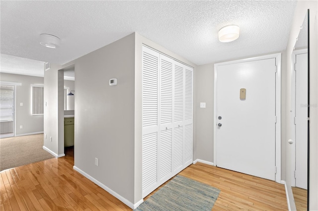 foyer entrance with baseboards, a textured ceiling, and light wood-style floors