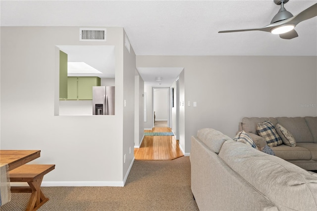 living area with light carpet, visible vents, baseboards, and a ceiling fan