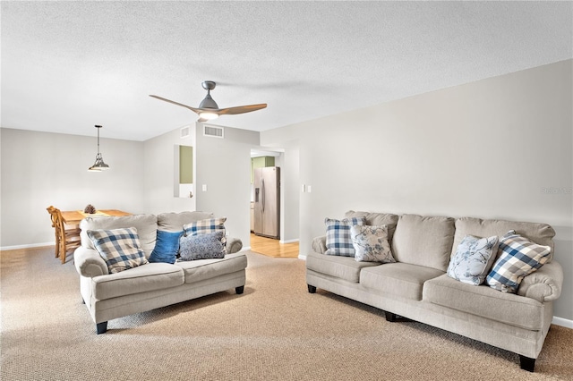 living room featuring a ceiling fan, light colored carpet, visible vents, and a textured ceiling