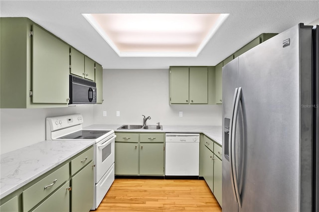 kitchen with light wood finished floors, green cabinetry, a tray ceiling, white appliances, and a sink