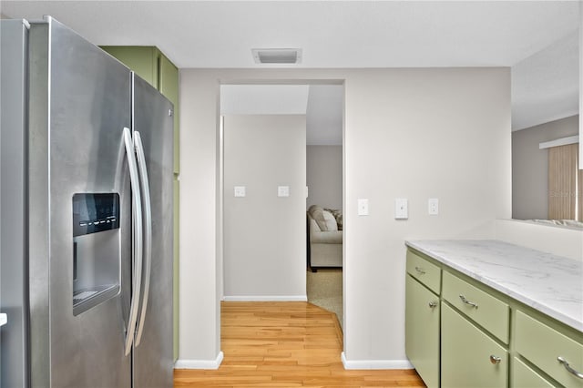 kitchen with baseboards, visible vents, stainless steel refrigerator with ice dispenser, green cabinets, and light wood-type flooring