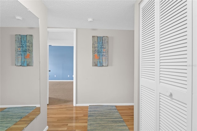 hallway featuring a textured ceiling, light wood-type flooring, and baseboards