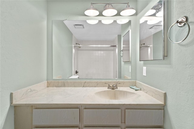 full bathroom featuring vanity, a textured wall, visible vents, and a shower with door