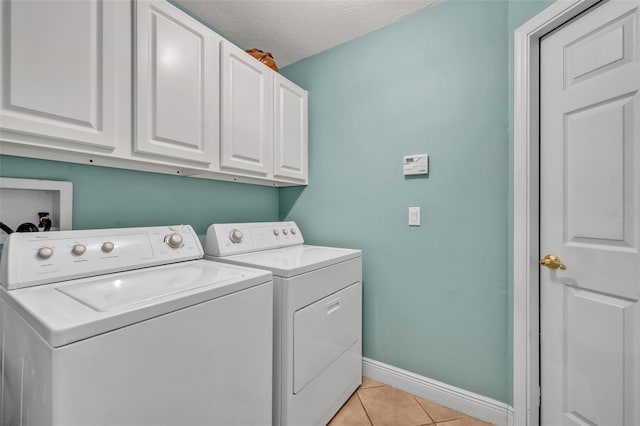 washroom with washing machine and clothes dryer, light tile patterned floors, cabinet space, a textured ceiling, and baseboards