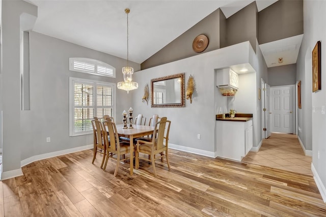 dining area featuring high vaulted ceiling, light wood-type flooring, a notable chandelier, and baseboards