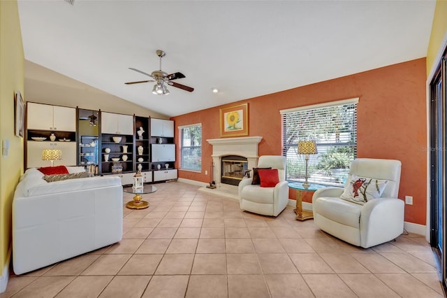 living area with light tile patterned floors, a ceiling fan, a glass covered fireplace, vaulted ceiling, and baseboards