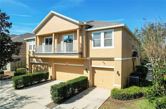 multi unit property featuring concrete driveway, a balcony, an attached garage, central air condition unit, and stucco siding