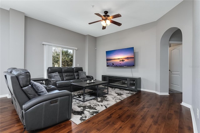 living room with arched walkways, wood-type flooring, a ceiling fan, and baseboards