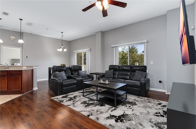 living room featuring ceiling fan with notable chandelier, wood finished floors, and baseboards