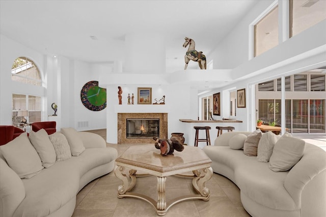 living area with a high ceiling, light tile patterned flooring, a glass covered fireplace, and visible vents