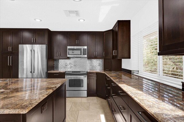 kitchen with visible vents, appliances with stainless steel finishes, dark stone countertops, dark brown cabinets, and backsplash